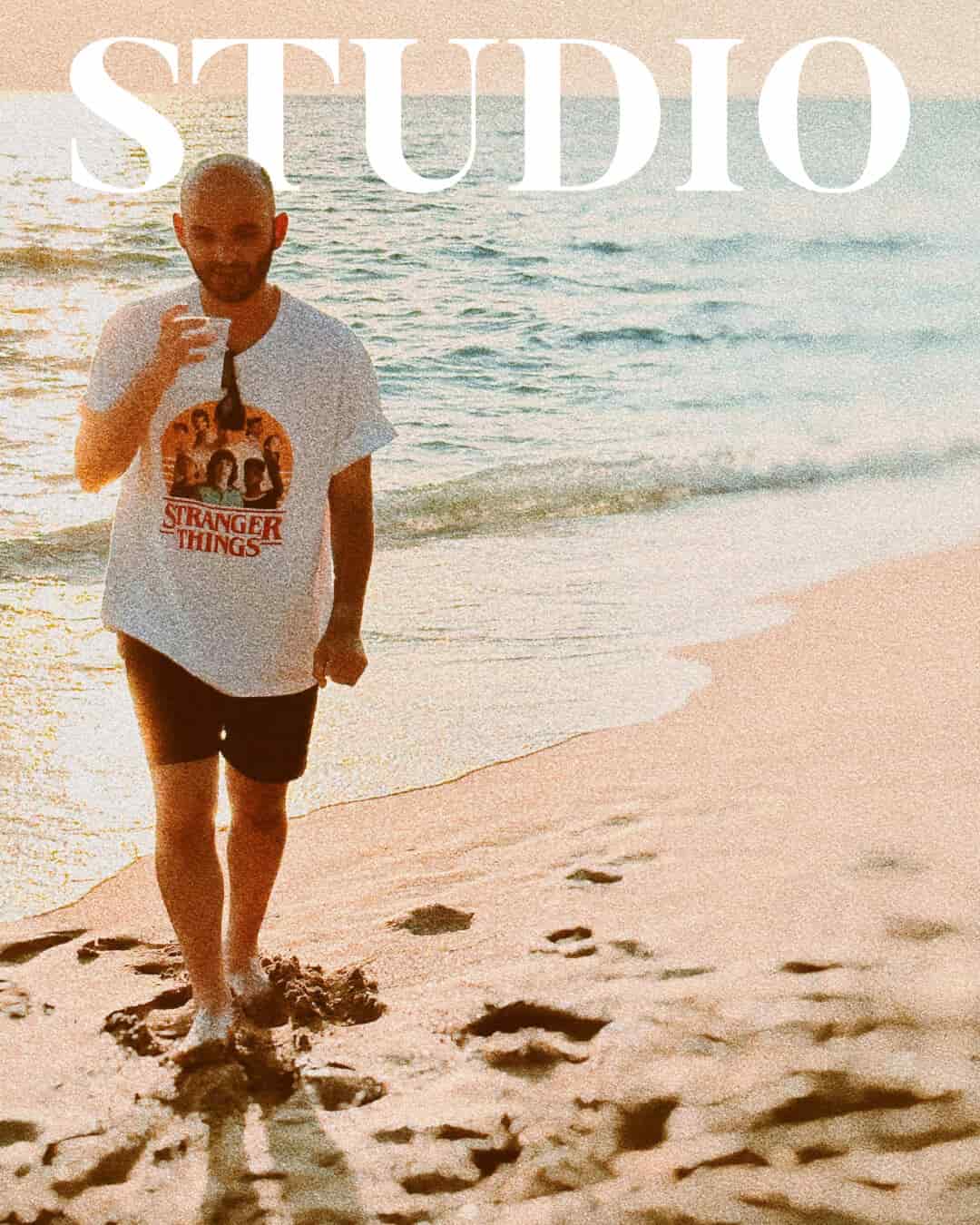 Mann in Stranger-Things-Shirt am Strand, "STUDIO" Überschrift. UX-Designer Christos Stavrou teilt Erfahrungen zur Selbstreflexion.