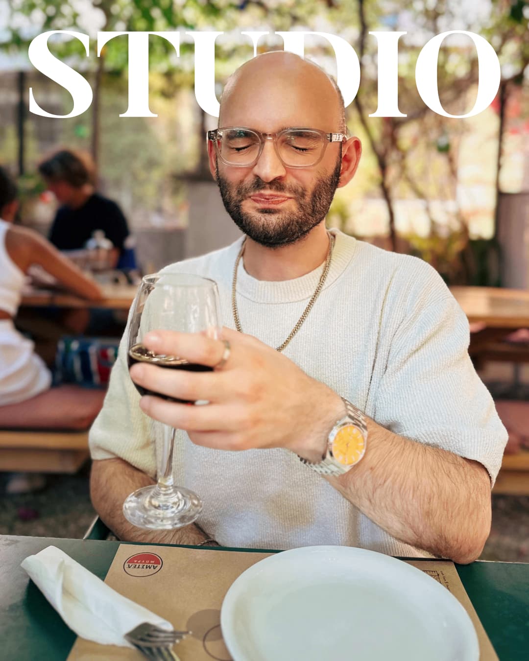 UX-Designer mit Brille und Glatze verzieht Gesicht beim trinken eines bitteren Glases Rotwein im Freien. Text "STUDIO" im Bild.