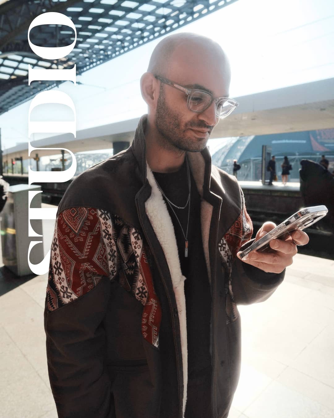 UX-Designer mit Smartphone am Bahnhof, "STUDIO" Schriftzug. Christos Stavrou teilt Erfahrungen zur Mehrwertschaffung im Business.