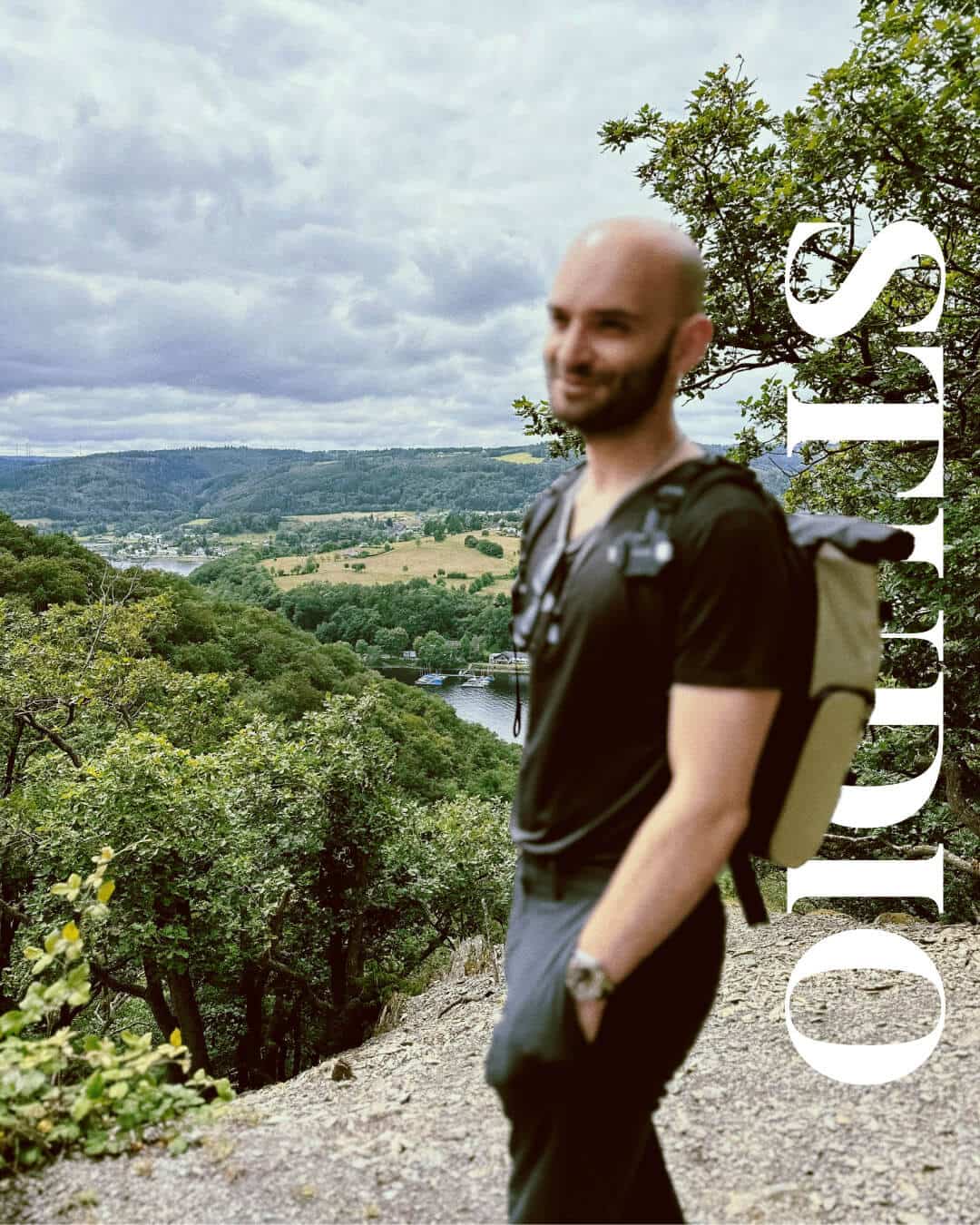 Lächelnder Mann mit Rucksack blickt auf weite Landschaft. Symbolisiert Fokus und Weitblick für Selbstständige, passend zum Thema Konzentration.